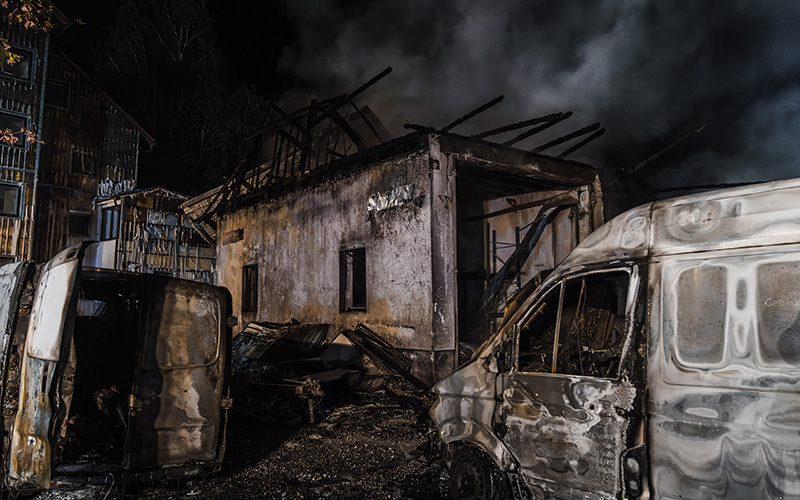 Verwüstetes Gebäude und Fahrzeuge nach einem Großbrand.